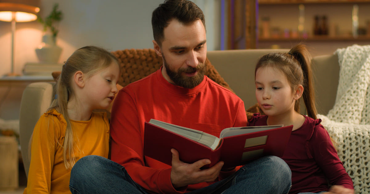 Tappe della lettura con un papà che legge un libro ai due figli mentre tutti sono seduti su un divano